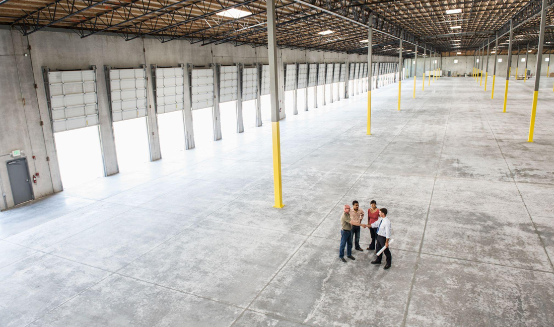 Four people discussing plans in a large, empty cold storage facility interior with high ceilings and multiple loading dock doors.